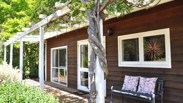 A wooden cabin with large windows, a bench, and a pergola.