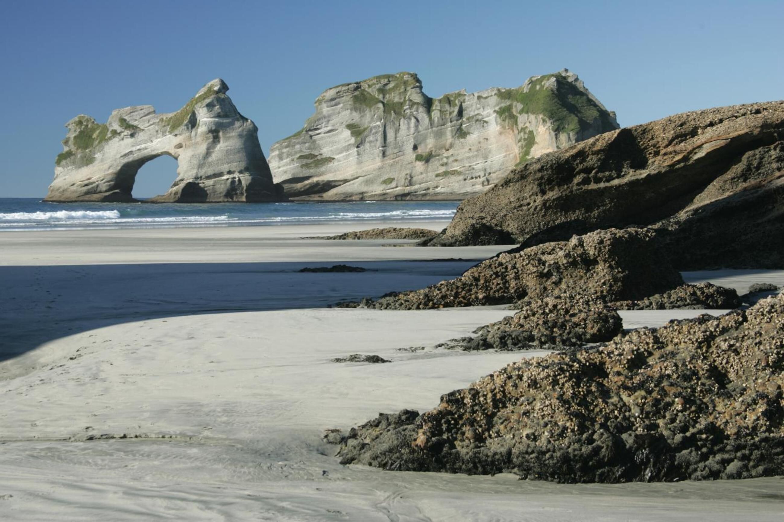 A beach with a natural rock formation and a clear sky.