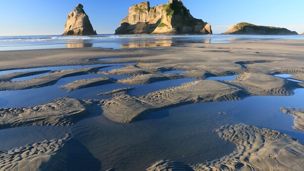 Una playa con grandes formaciones rocosas y una superficie de arena húmeda.