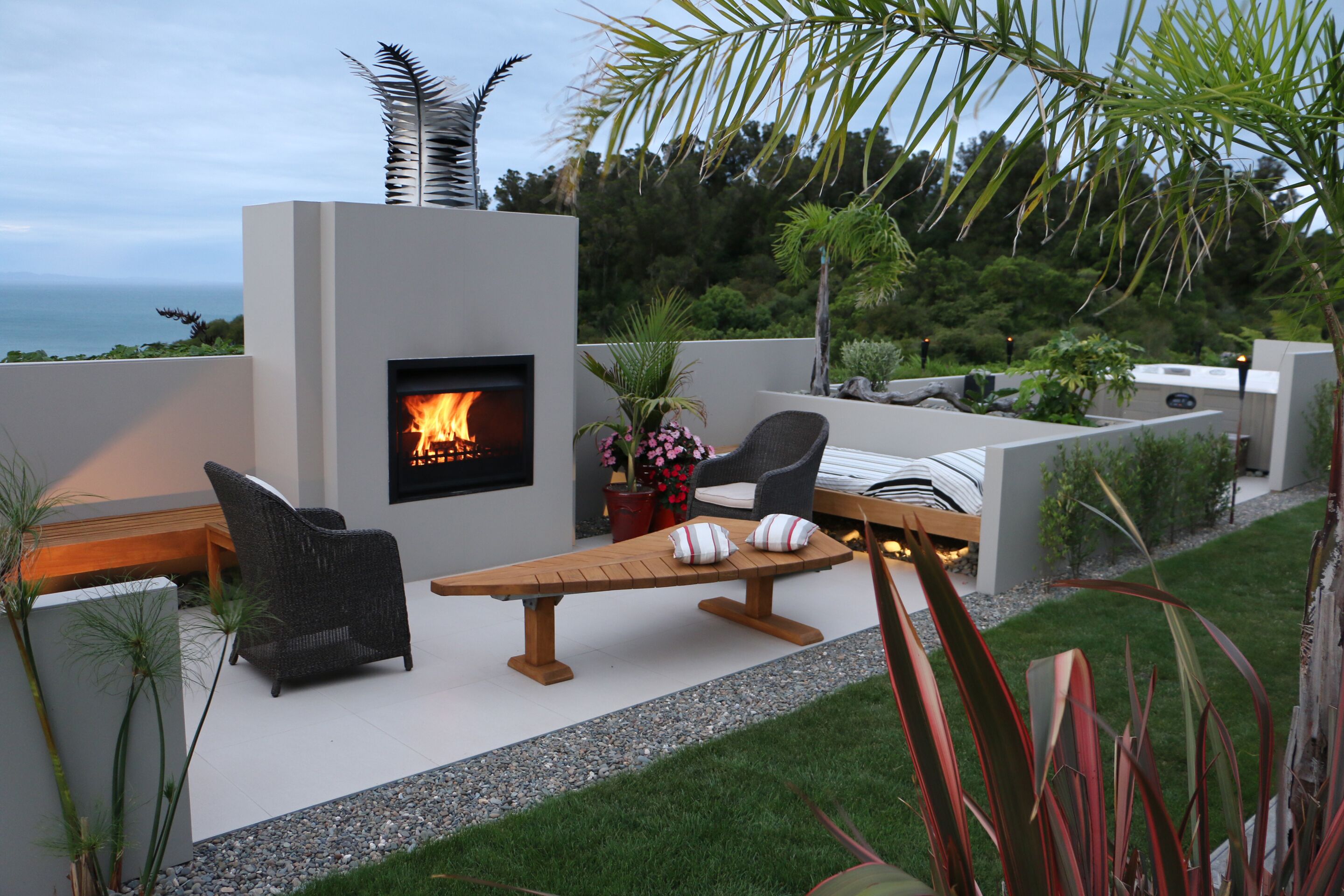A modern outdoor patio with a built-in fireplace, seating, and a view of the ocean.
