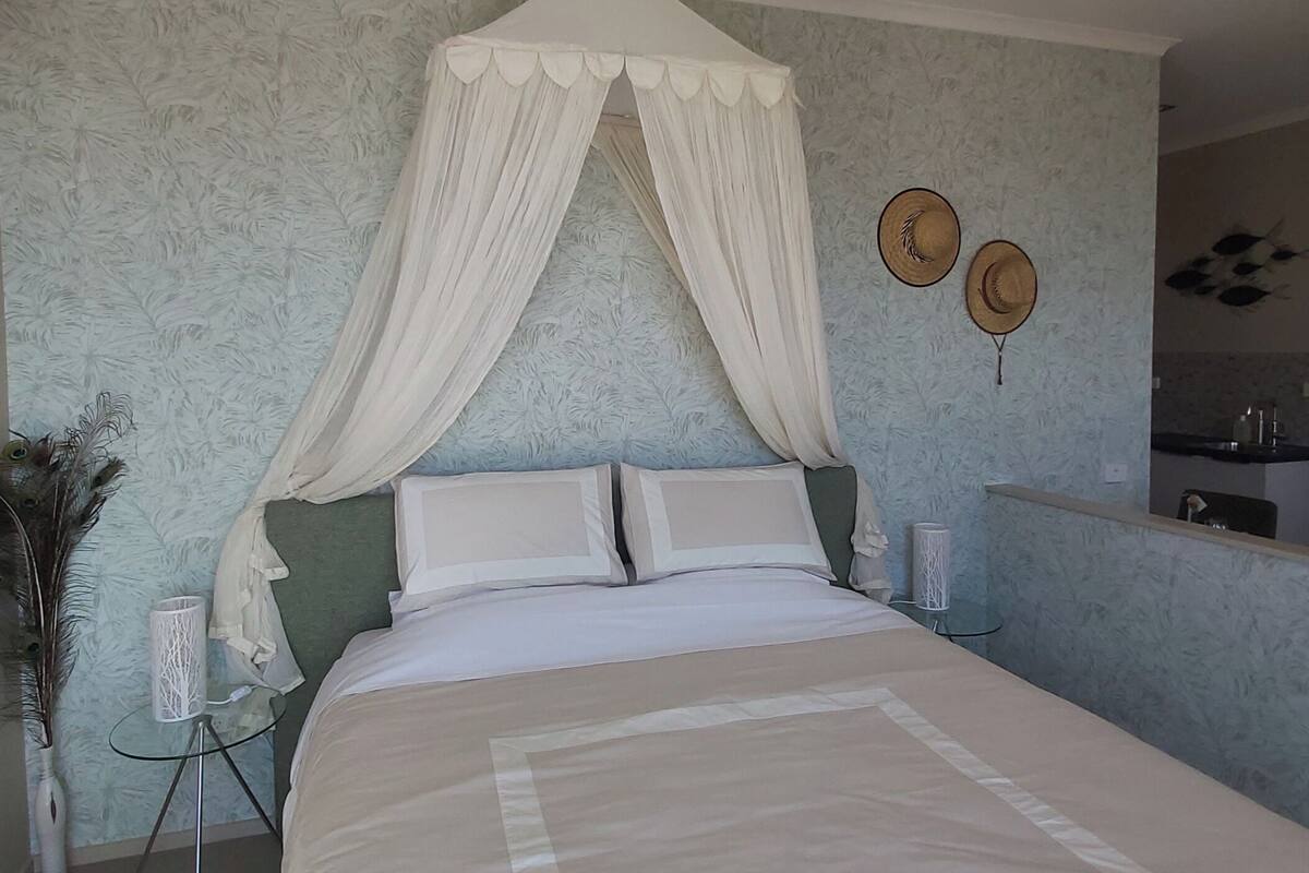 A bedroom with a canopy bed, a small bedside table with a lamp, and a mirror on the wall.