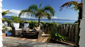 Un patio con mobiliario de mimbre, una mesita y vistas a un lago y montañas.