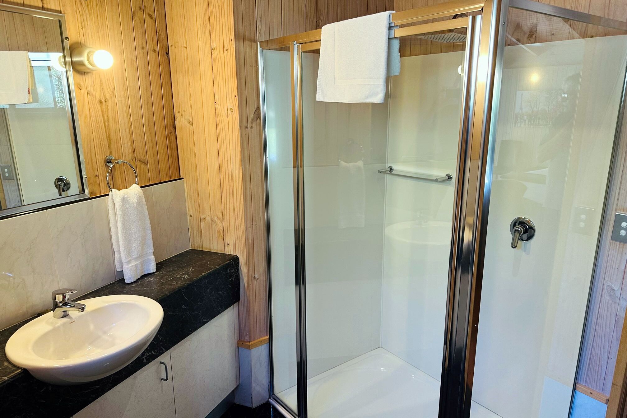 A modern bathroom with a glass-enclosed shower, a white sink, and a wooden vanity.