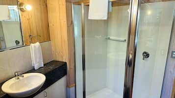 Ein modernes Badezimmer mit einer Duschkabine aus Glas, einem weißen Waschbecken und einem hölzernen Waschtisch.