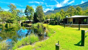 A lakeside lodge with a grassy lawn, a pond, and a mountain backdrop.