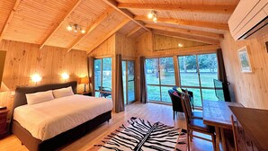 A wooden cabin bedroom with a bed, a table, and a view of the outdoors.