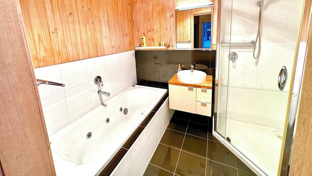 Un baño moderno con pared de madera, una bañera, un lavamanos y una cabina de ducha de vidrio.