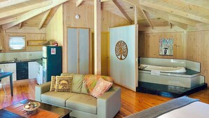 A cozy cabin interior with a dining area, a sofa with decorative pillows, a kitchenette, a bathroom with a bathtub, and a large window.