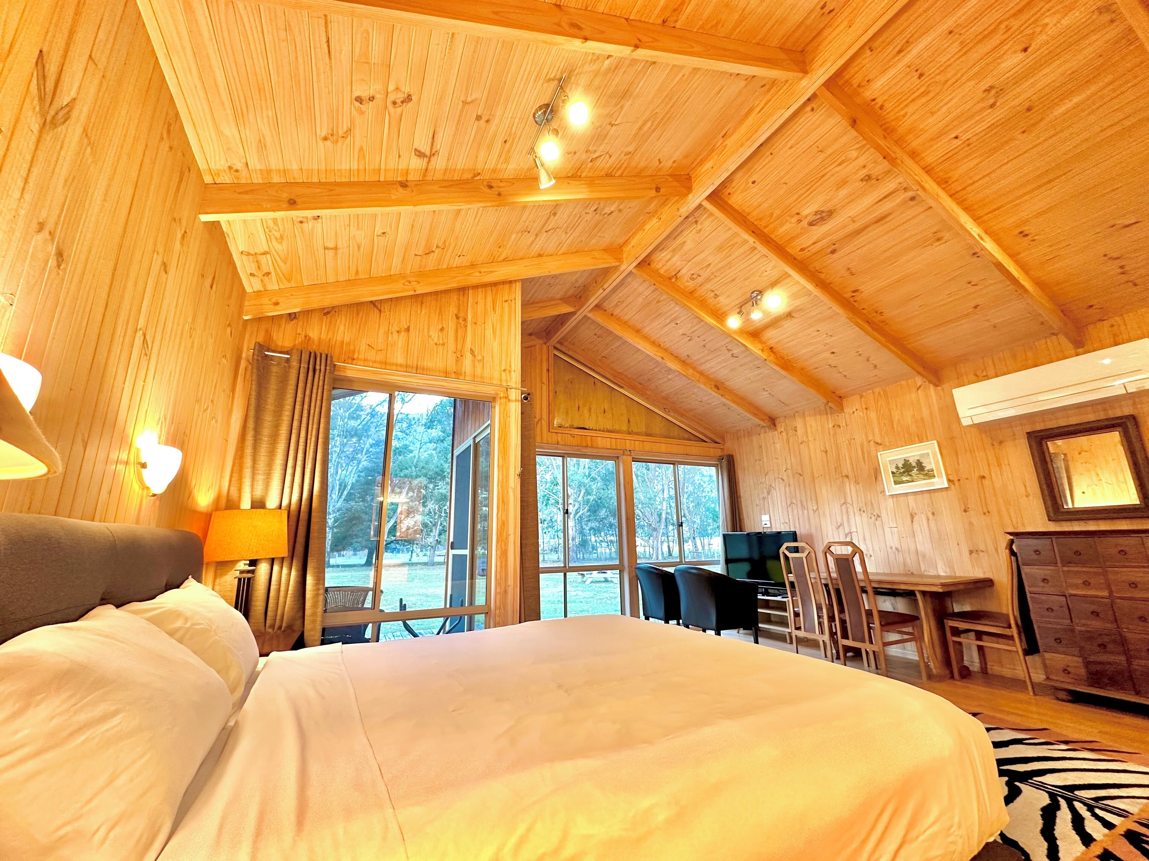A wooden cabin interior with a bed, a desk, and a dining area.