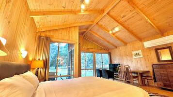 Interior de una cabaña de madera con una cama, un escritorio y una zona de comedor.