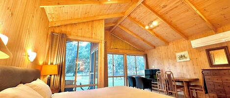 A wooden cabin interior with a bed, a desk, and a dining area.
