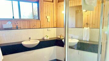 Un baño con paneles de madera, un lavamanos blanco, una encimera negra y una cabina de ducha de vidrio.