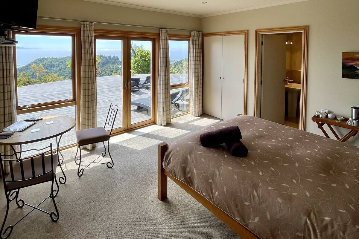 Un dormitorio con cama, escritorio y silla. Hay cortinas y vistas al exterior.