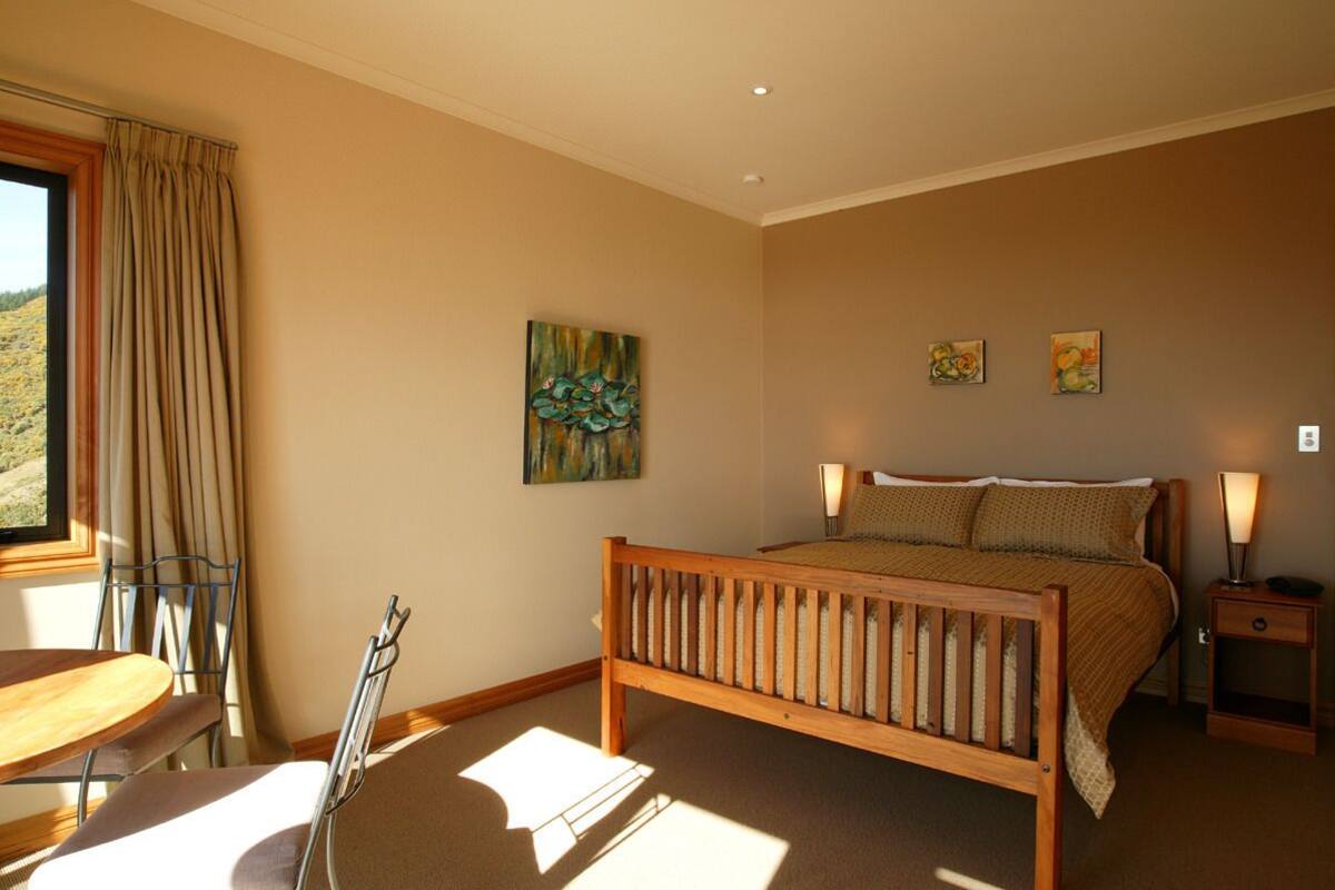 Un dormitorio con una cama de madera, dos lámparas de noche, un ventanal con cortinas y un cuadro en la pared.