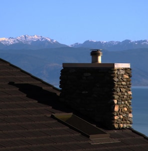 A stone chimney on a rooftop with a view of snow-capped mountains in the background.