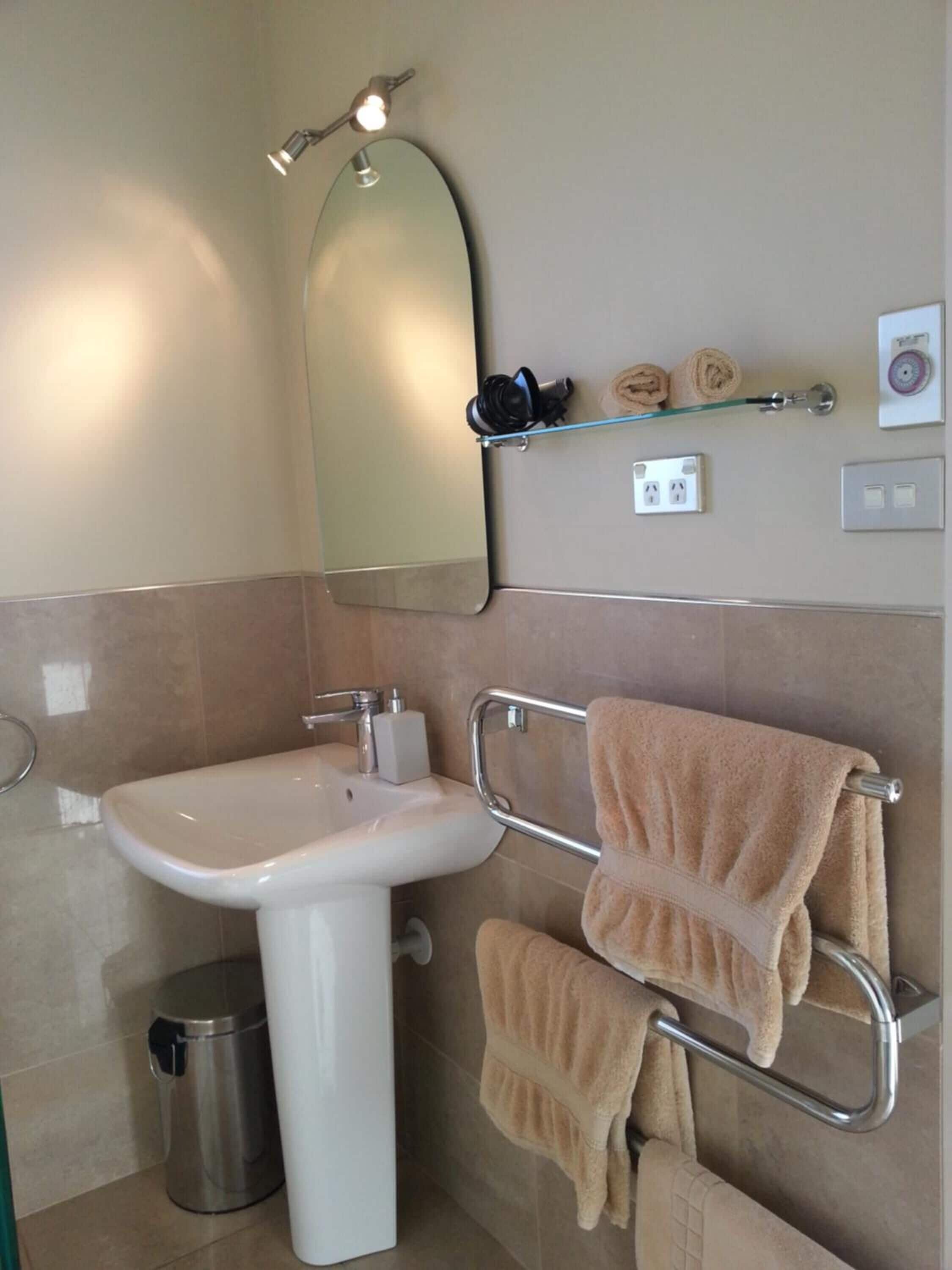 Un baño con lavamanos, espejo, perchero y una pequeña estantería con toallas.