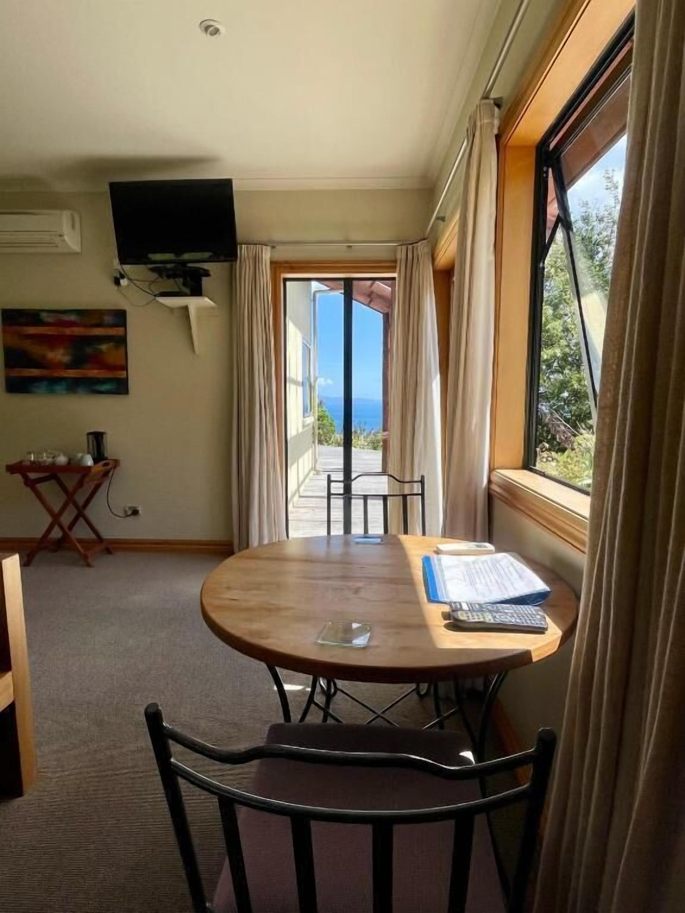 A room with a round table, chairs, a television, and a view of the outdoors.