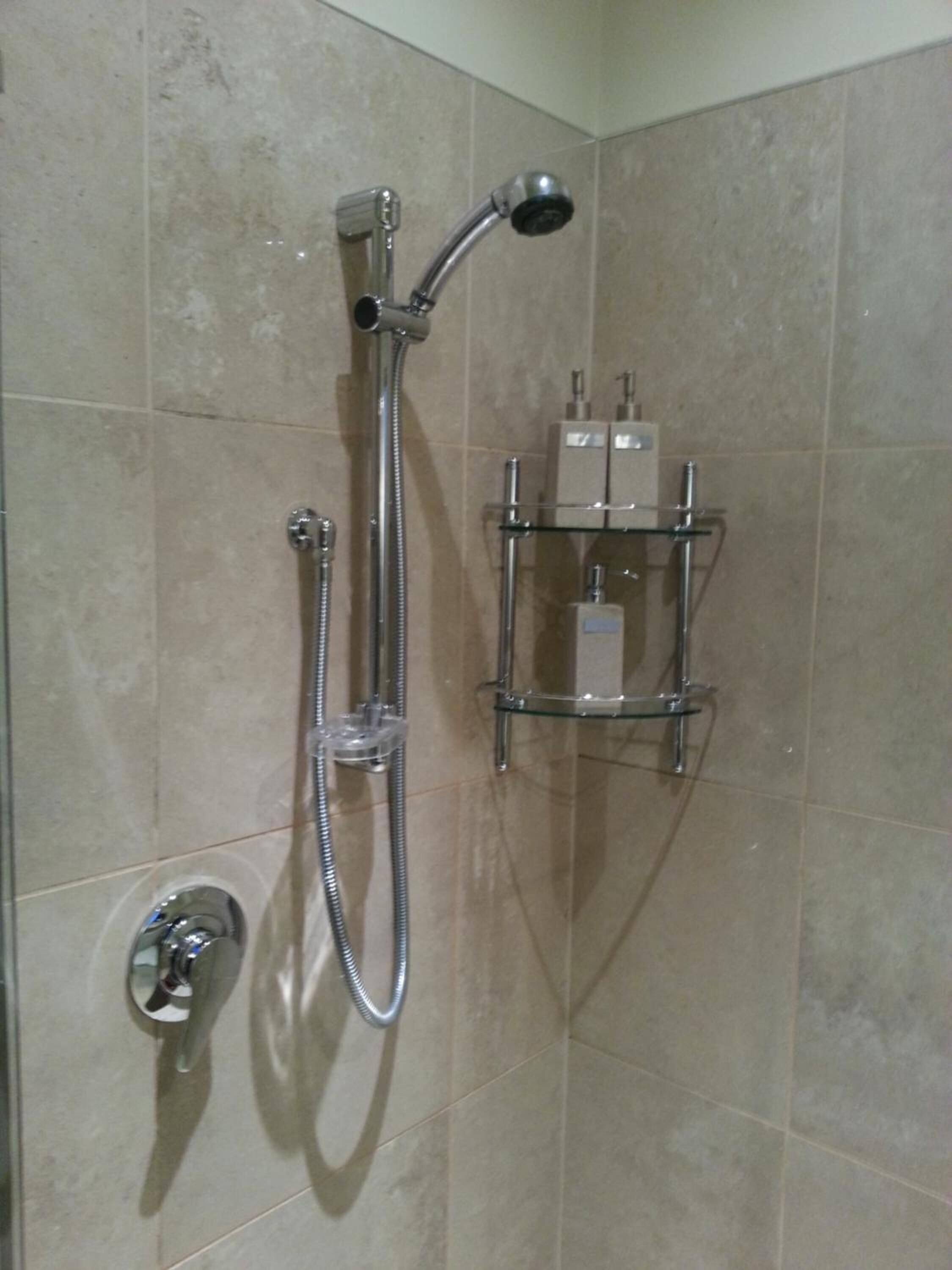 A shower with a handheld showerhead and a wall-mounted faucet.