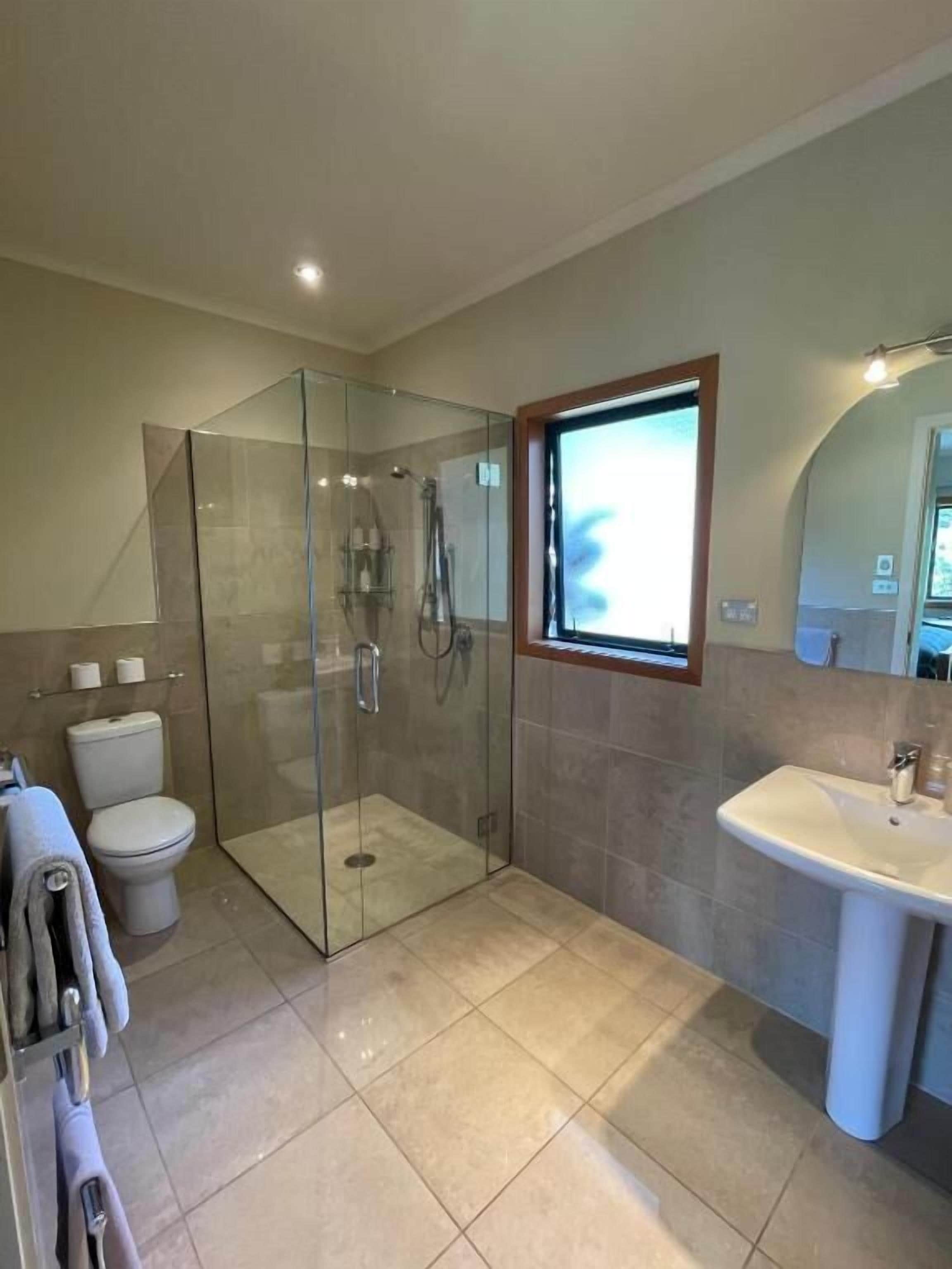 A modern bathroom with a glass-enclosed shower, a toilet, and a sink.