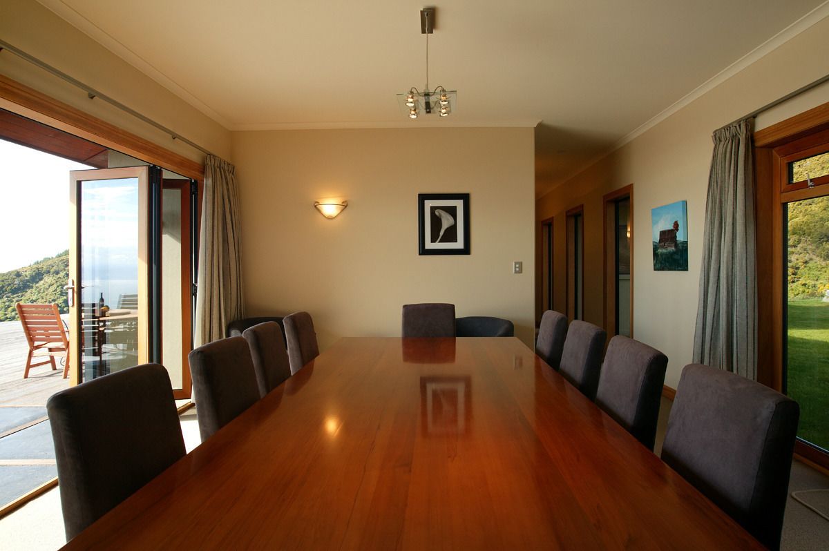 Un salón de conferencias con una larga mesa de madera, seis sillas, una araña y ventanas grandes con cortinas.