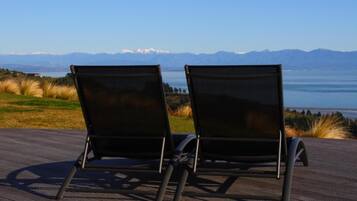 Two black lounge chairs on a wooden deck with a view of mountains and a lake.