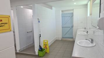 Un baño público con paredes de azulejos blancos, varios lavamanos y una zona de ducha.