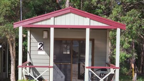 A small, single-story cabin with a red roof and a number '2' sign. It has a glass door and a small porch with a bench.