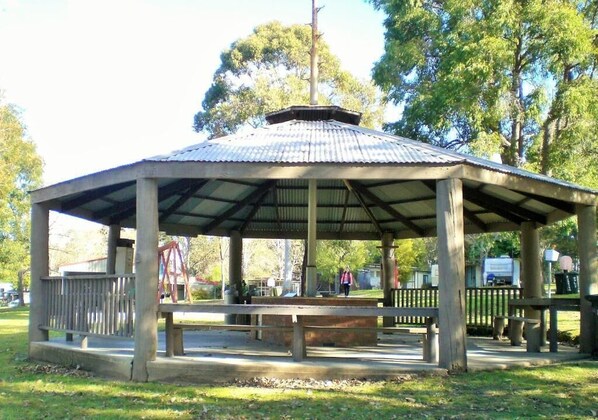 A gazebo with a metal roof and wooden pillars, surrounded by grass and trees. - Mallacoota's Shady Gully Caravan Park (Mallacoota)