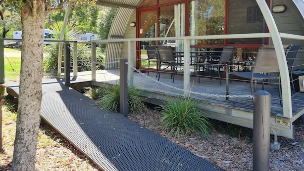 A covered outdoor seating area with tables and chairs, surrounded by trees and a metal fence.
