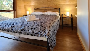 A bedroom with a bed, bedside lamps, and a view of greenery outside.