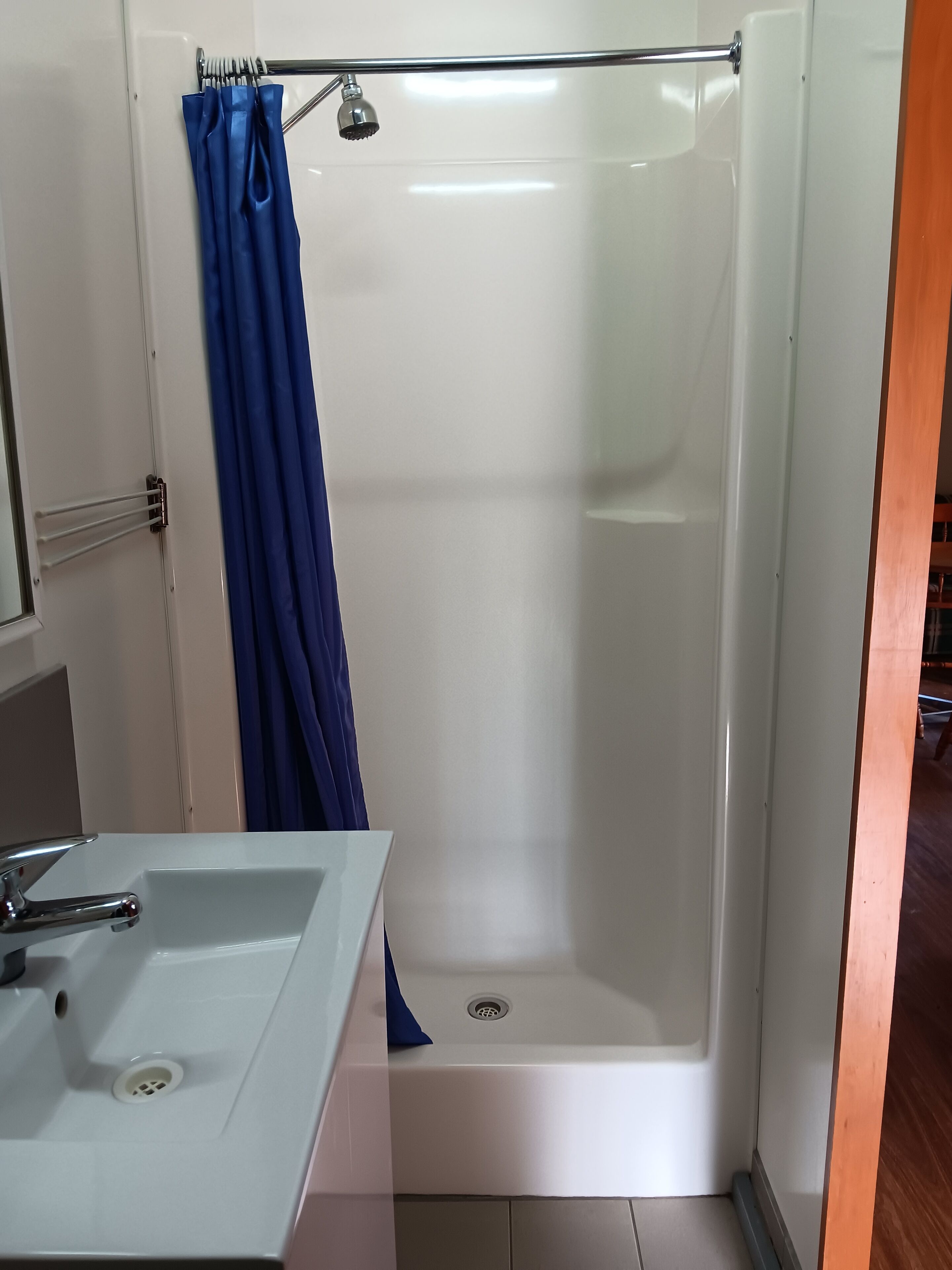 A bathroom with a white sink, a shower with a blue curtain, and a wooden floor.