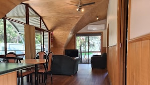 A spacious interior with a high ceiling, wooden flooring, and large windows offering a view of the outdoors.