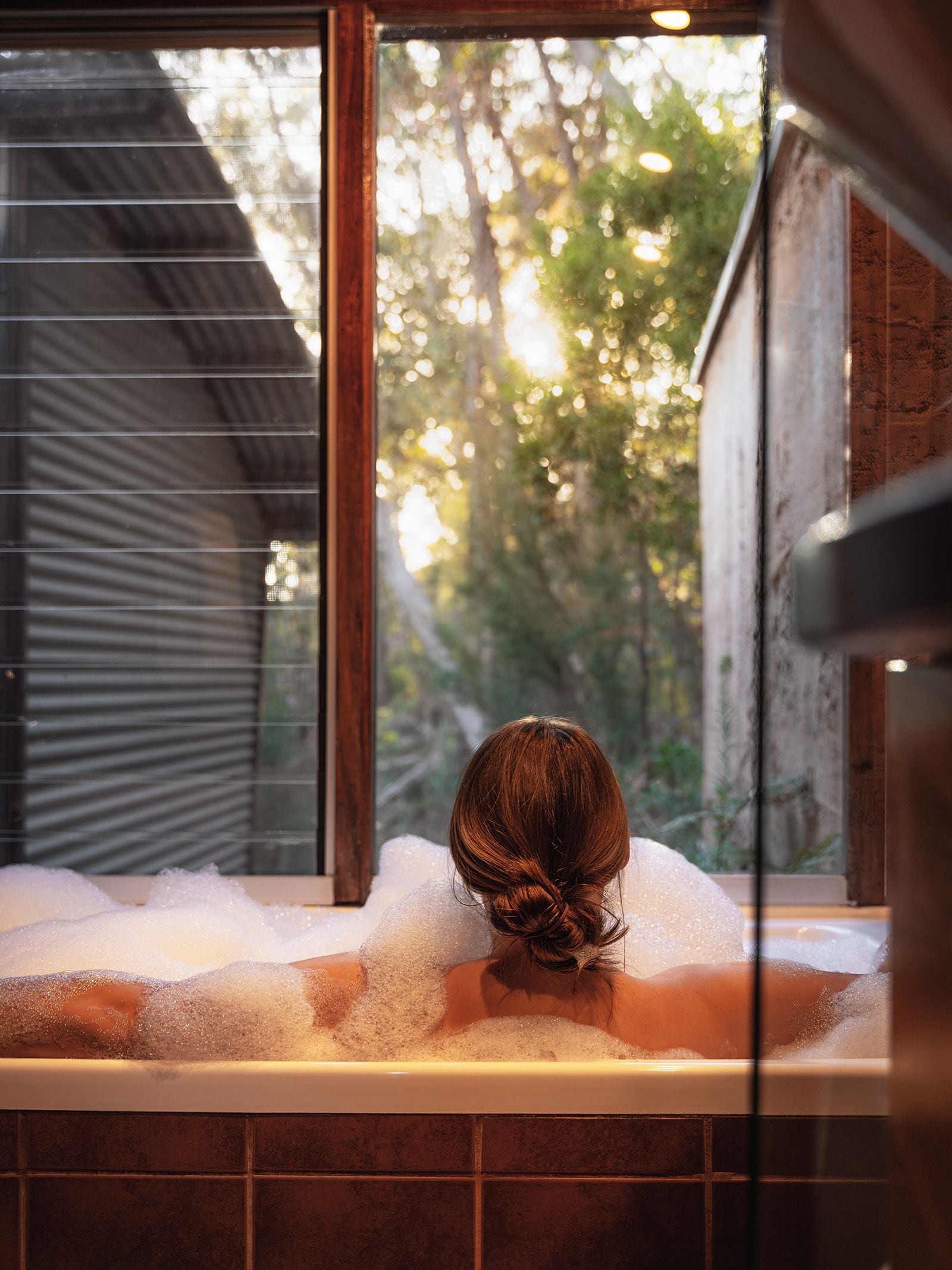 A person in a bathtub with a window view of trees.