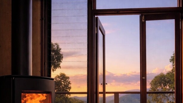 A room with a wood-burning stove, a sliding glass door leading to a balcony with a scenic view. - The Odd Frog (Bright)