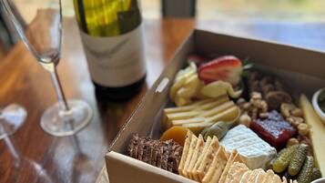 Una mesa de madera con una botella de vino, una copa y una tabla de fiambres con varios quesos, carnes y galletas.