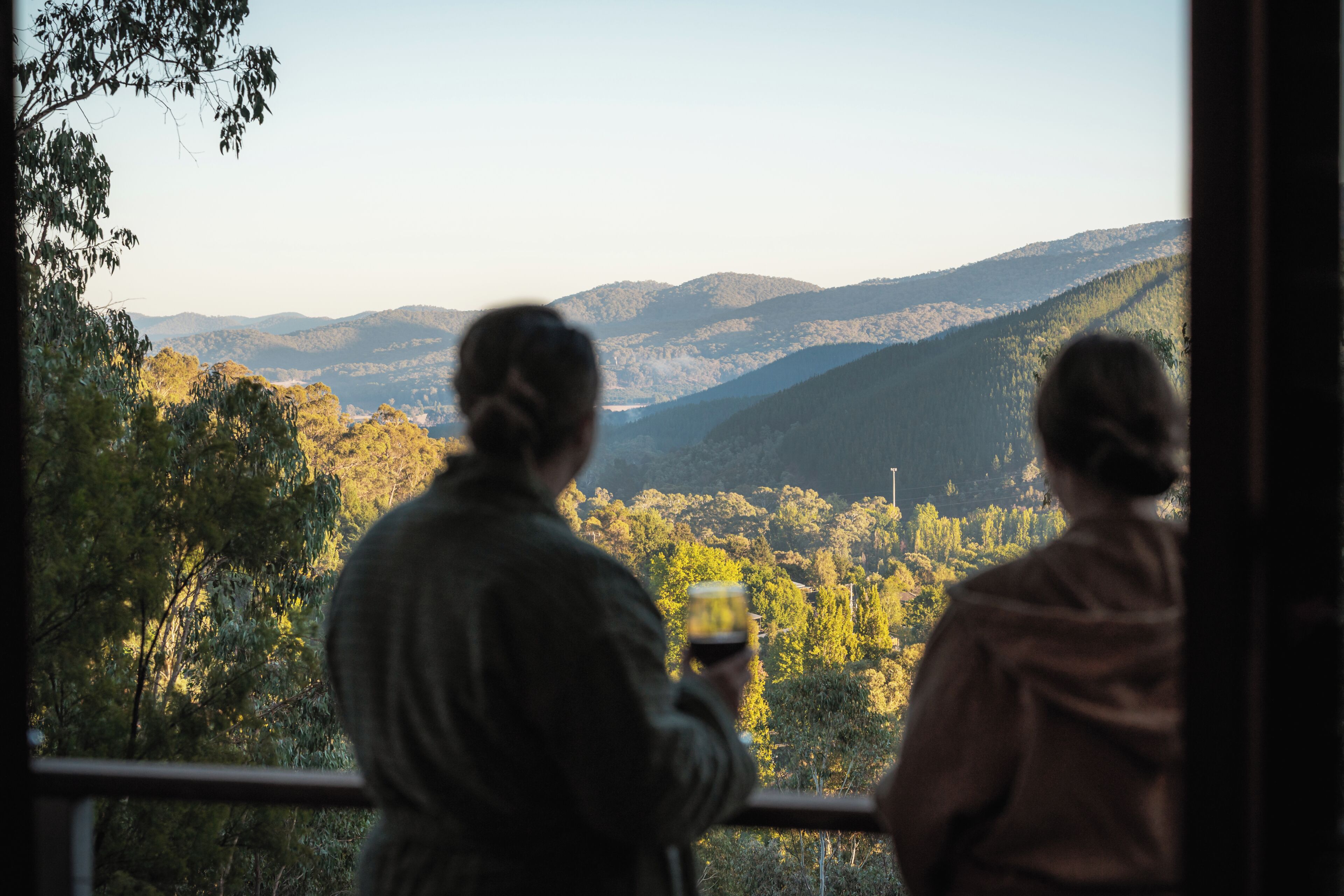 Two people overlooking a mountainous landscape from a balcony.