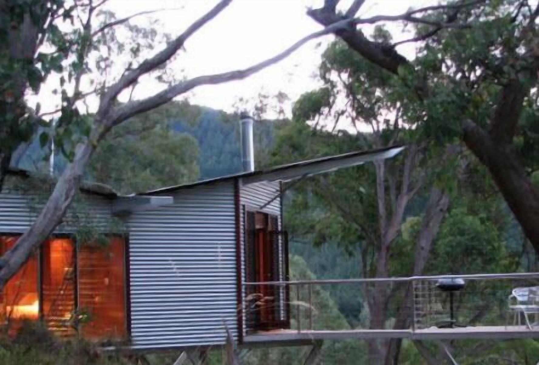 A modern, metal-framed house with a balcony overlooking a forested area.