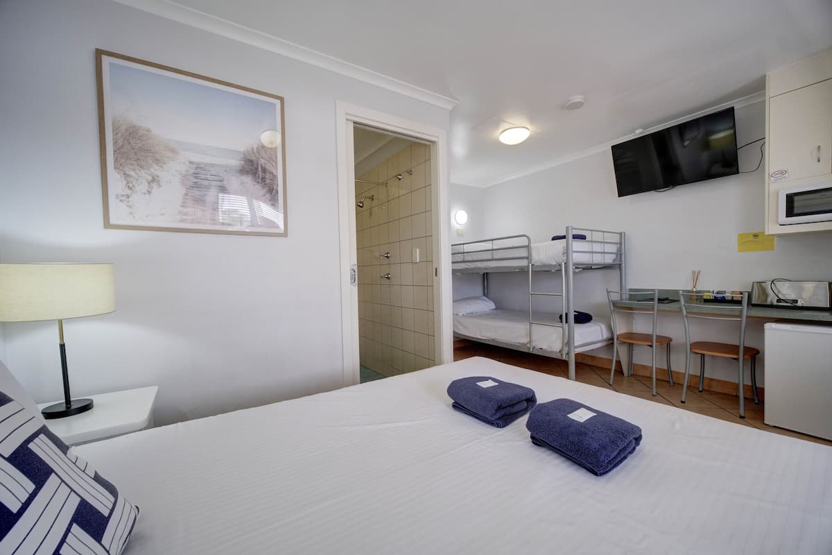 A hotel room with a bed, a desk, a TV, and a kitchenette.