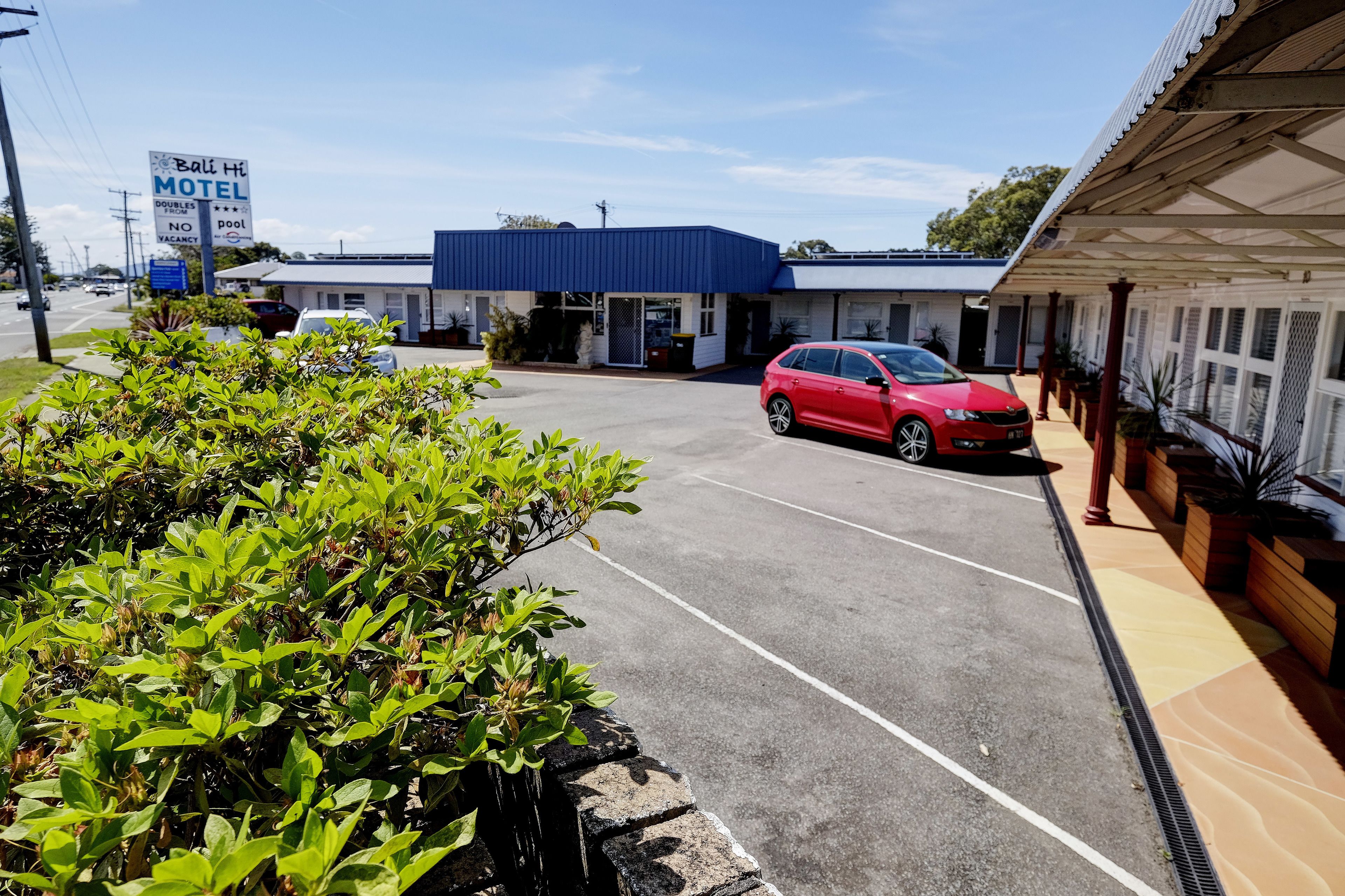 Un motel con techo azul, un coche rojo estacionado adelante y un letrero que anuncia una piscina.