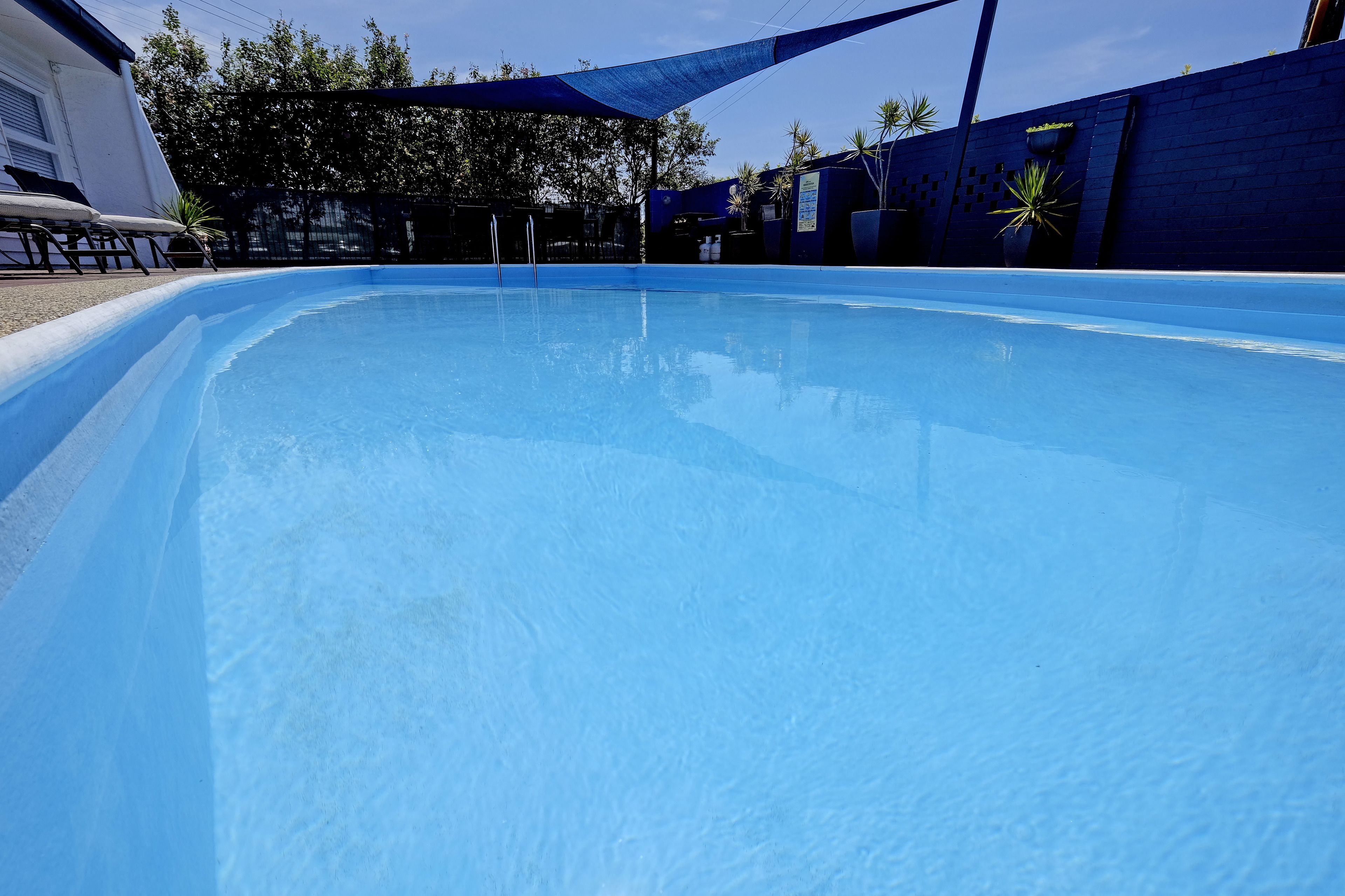 En klarblå pool med ett område som ger skugga, omgiven av en blå vägg och några krukväxter.