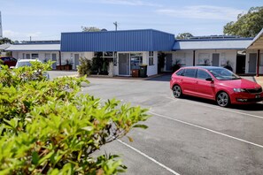 A parking lot with a red car parked in front of a building with a blue roof.