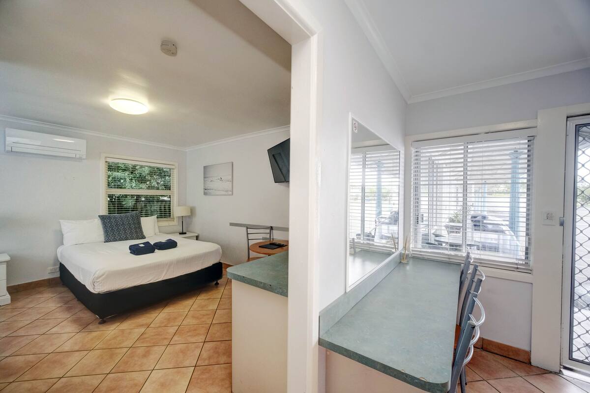 A bedroom with a bed, bedside table, and a window with blinds.