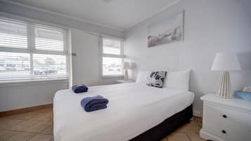 A hotel room with a large bed, white walls, a painting, and a window with blinds.