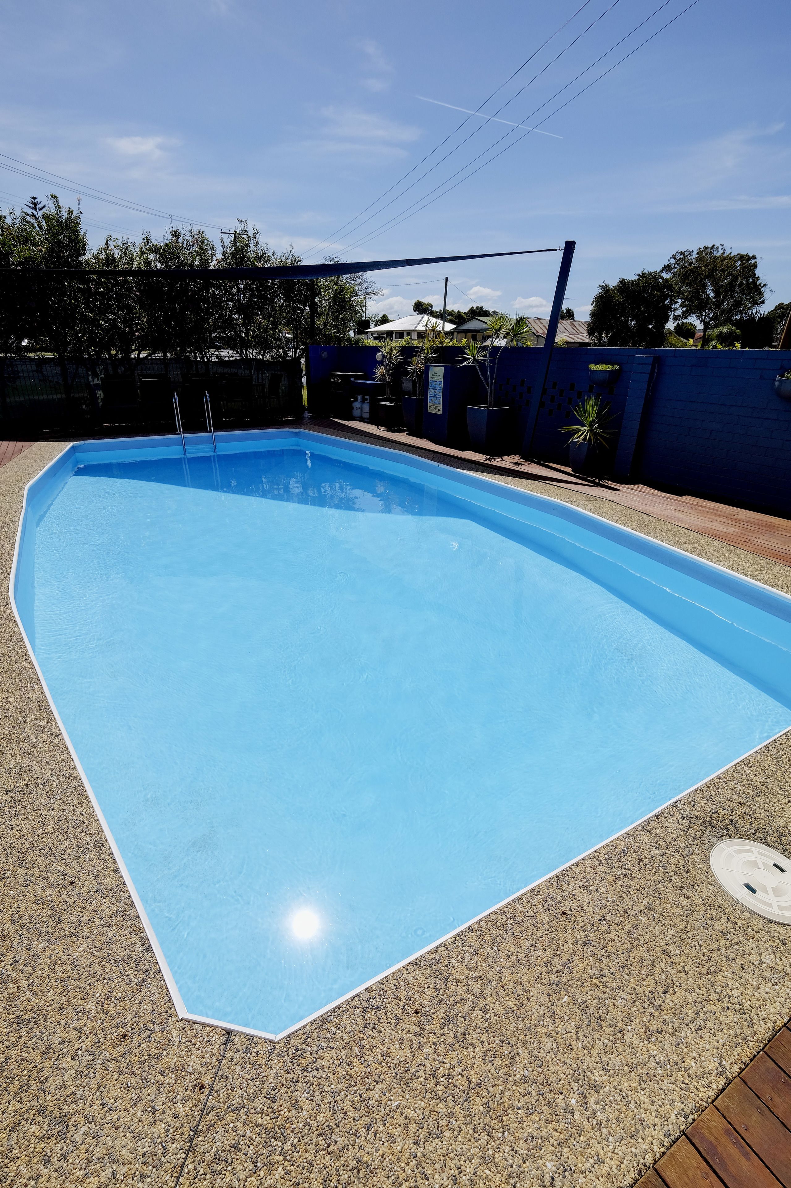 A rectangular swimming pool with a blue interior, surrounded by a pebble-textured deck.