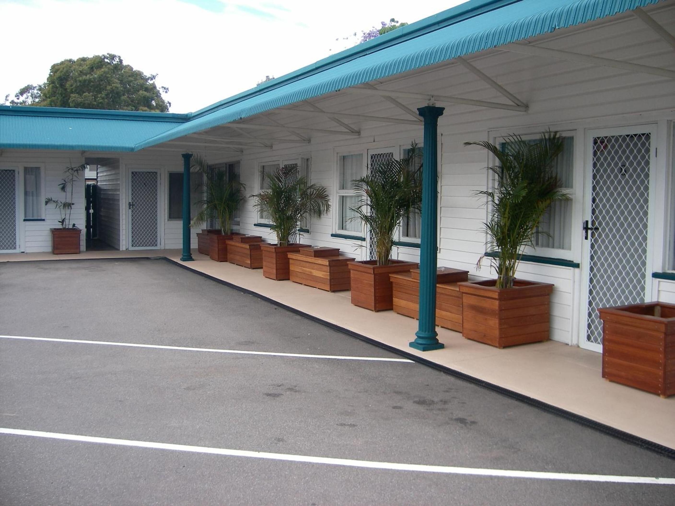A hotel with a covered outdoor area, wooden planters with plants, and a clear sky.