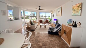 Un espacio habitable amplio con un sofá, sillas, una mesa de centro, un televisor y un balcón con vista a la ciudad.