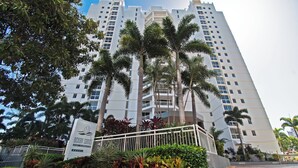 Un hotel alto con varios pisos, palmeras y un letrero que dice 'Ocean Sands'.