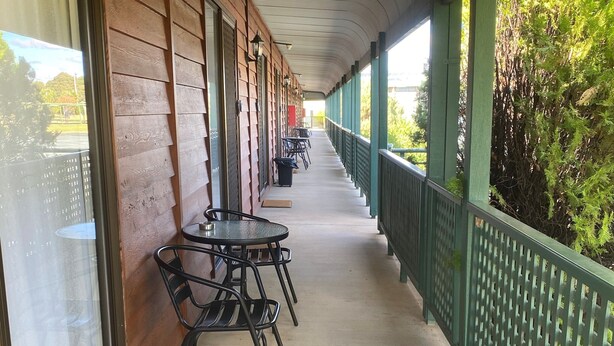A covered outdoor area with a row of tables and chairs, wooden walls, and a green railing.