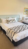 Una cama bien hecha con una colcha estampada, una mesita de noche con lámpara y un cuadro en la pared.