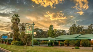 A rural motel with a green roof, surrounded by trees and a sign advertising a motor inn and bowling club.